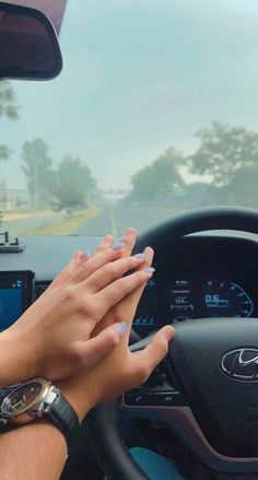 two hands on the steering wheel of a car, while another person holds their hand out