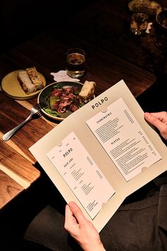 a person sitting at a table with some food on top of it while holding up a menu