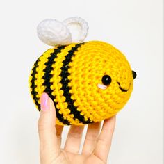 a hand holding a small crocheted yellow and black ball with a white cloud on top