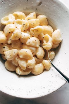 a white bowl filled with macaroni and cheese on top of a table next to a fork