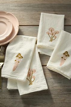 four white towels with gold embroidered flowers on them next to a pink plate and fork