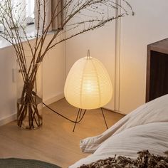 a white lamp sitting on top of a bed next to a vase with branches in it