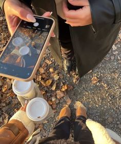 two people are sitting on the ground with their cell phones and cups in front of them