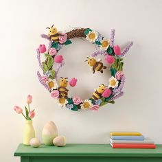 a wreath made out of crocheted flowers and bees on a green table next to a vase with pink tulips