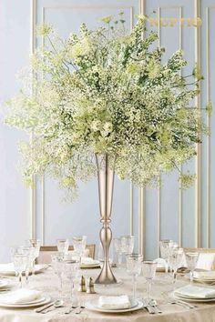 a tall vase filled with lots of white flowers on top of a dining room table