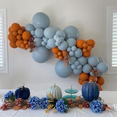 an arrangement of balloons and pumpkins on a white table cloth with blue hydrangeas