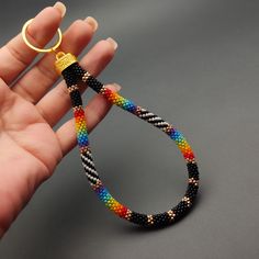 a hand holding a colorful beaded bracelet with a gold ring on it's end