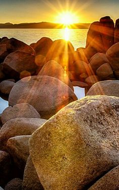 the sun is setting over some rocks by the water