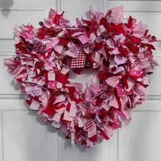 a heart shaped wreath hanging on the side of a white door covered in pink and red tissue paper