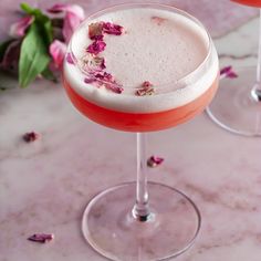 two glasses filled with drinks sitting on top of a marble table next to pink flowers