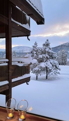 two wine glasses are sitting on a table in front of a window overlooking the snow covered mountains