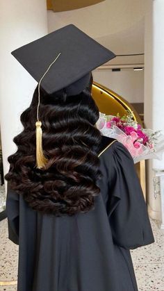 a woman wearing a graduation cap and gown with long curly hair in the middle of her body