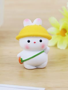 a small white rabbit figurine with a yellow hat and carrot in its hand