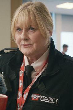 a woman with blonde hair wearing a security uniform and holding a cup in her hand