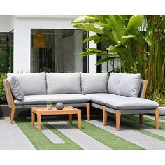 a couch and coffee table sitting on top of a grass covered patio area with potted plants