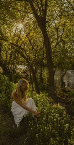 a woman is sitting in the grass near some trees