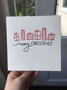 someone is holding up a card that says merry christmas with presents on it in front of a window