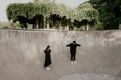 two people are standing on the edge of a skateboard ramp and one person is holding his arms out