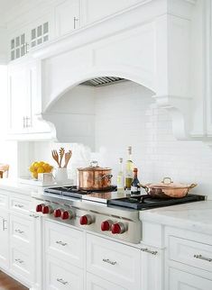 a kitchen with white cabinets and red knobs on the stove top, along with pots and pans