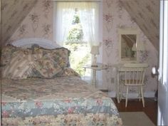 a bed sitting under a window next to a white table and chair in a bedroom