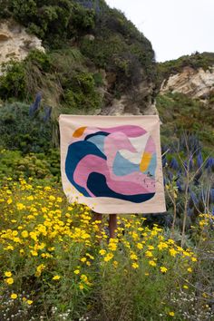 a sign in the middle of a field with wildflowers and cliffs behind it