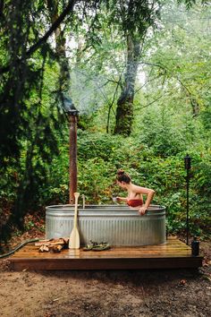 a woman in a bathing suit is taking a bath in a metal tub with a wooden pole