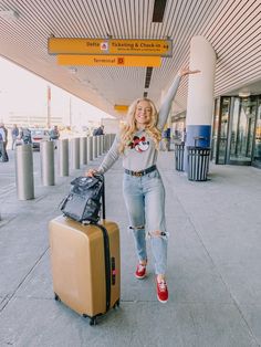 a woman in ripped jeans and red shoes is holding her hand up as she stands next to two suitcases