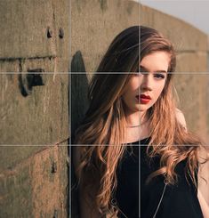 a woman with long hair leaning against a wall and looking at the camera while wearing red lipstick