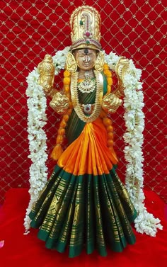 an idol is displayed in front of a red backdrop with white flowers and greenery