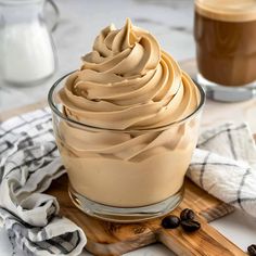 a glass bowl filled with whipped cream on top of a wooden cutting board next to two cups of coffee