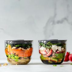 two mason jars filled with salads on top of a white counter next to an apple