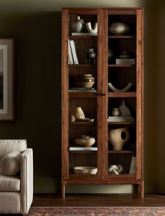 a living room with a chair and bookcase filled with vases on top of it