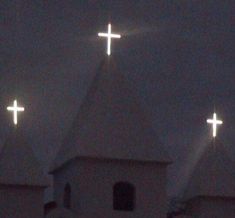 three white crosses on top of a church steeple in the dark sky at night