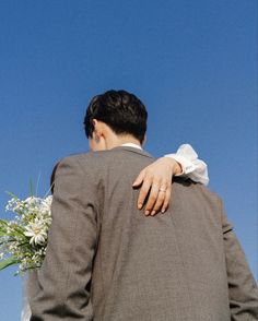 a man in a suit and tie holding a woman's back as they stand under a clear blue sky