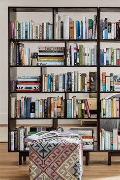 a bookshelf filled with lots of books next to a footstool on top of a hard wood floor