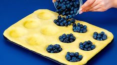 a person scooping blueberries into a muffin tin with yellow icing on a blue background