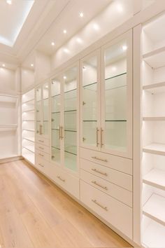 an empty white closet with glass doors and shelves on the wall, along with hardwood flooring