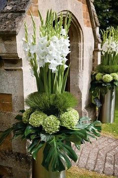 two vases with flowers and greenery in front of an old stone building on the grass