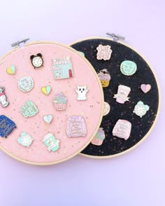 two embroidery hoops decorated with pins and magnets, one is pink and the other is black