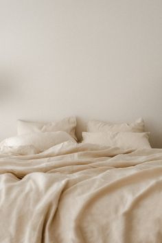 an unmade bed with white sheets and pillows in a small room next to a lamp