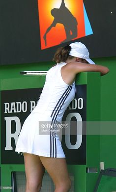 a woman in white dress leaning against a green wall with her hand on the back of her head