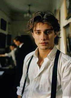 a young man with suspenders and a white shirt is standing in front of a group of people