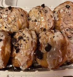 donuts covered in icing and sprinkled with chocolate chips, sitting in a plastic container