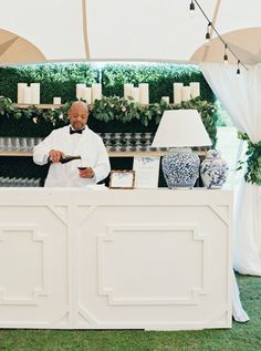 a man standing behind a counter at a wedding with candles on the wall and greenery in the background