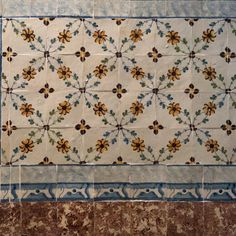 an old tiled wall with blue and yellow flowers on the border, next to a tile floor