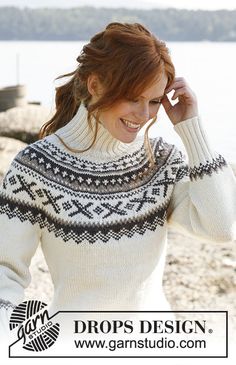 a woman sitting on top of a wooden bench next to the ocean wearing a sweater