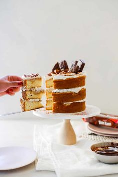 someone is holding a piece of cake on a plate with the rest of the cake in front of them