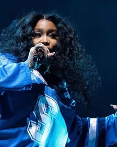 a woman with long black hair wearing a blue jacket and holding her hands out in front of her face