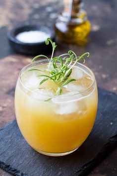 a glass filled with lemonade sitting on top of a black slate coaster and garnished with small green sprigs