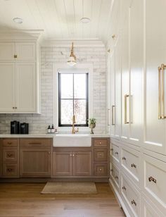 a kitchen with white cabinets and wood floors, along with a large window that looks out onto the outdoors